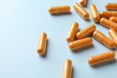 Açık mavi arka planda zerdeçal kapsülleri, yakın plan. Metin için boşluk