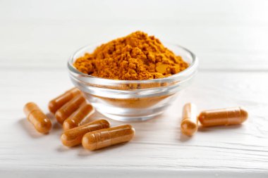 Beyaz ahşap masanın üzerinde zerdeçal kapsülleri ve toz, yakın plan.