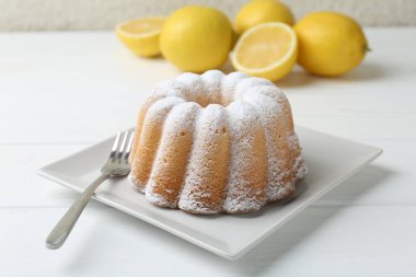 Beyaz ahşap masada pudra şekerli ve çatallı leziz limonlu pasta, yakın plan.