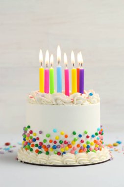 Rengarenk şekerli nefis bento keki ve beyaz masada yanan mumlar, yakın plan.