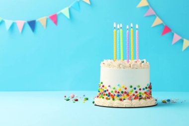 Renkli şekerli nefis bento keki ve açık mavi masada yanan mumlar. Metin için boşluk