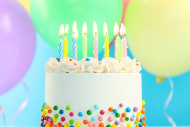 Enfes bento keki serpiştirilmiş, yanan mumlar ve açık mavi arka planda renkli balonlar, yakın plan.