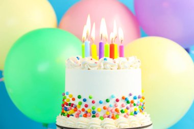 Enfes bento keki serpiştirilmiş, yanan mumlar ve açık mavi arka planda renkli balonlar, yakın plan.