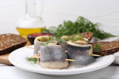 Zeytinli lezzetli ringa dürümleri, beyaz ahşap masada dereotu ve ekmek, yakın plan.