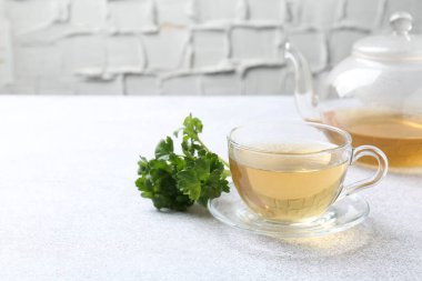 Cam bardakta romatik bitki çayı, taze maydanoz ve açık gri masada çaydanlık, yakın plan. Metin için boşluk