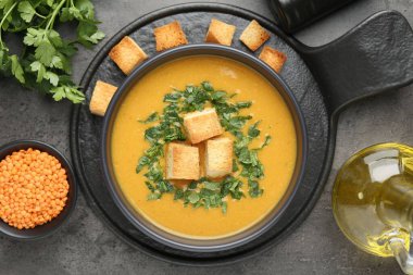 Lezzetli mercimek kremalı çorba. Gri masadaki kızarmış ekmeklerle servis ediliyor.