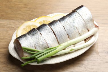 Limon dilimleri ve ahşap masada yeşil soğanlı lezzetli ringa balıkları.