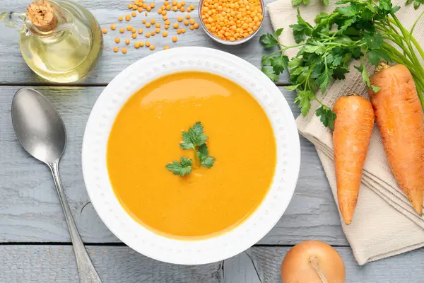 Gri ahşap masada servis edilen lezzetli mercimek kremalı çorba.