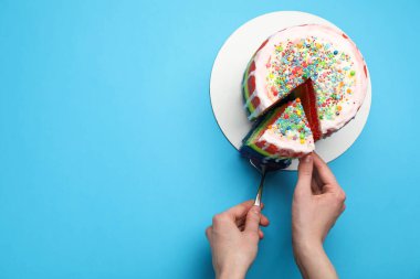 Açık mavi masada spatulayla lezzetli bir gökkuşağı pastası yiyen bir kadın. Metin için boşluk