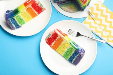 Açık mavi masada servis edilen leziz gökkuşağı pastasından parçalar.