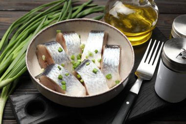 Siyah ahşap masada servis edilen taze soğanlı lezzetli ringa balıkları.