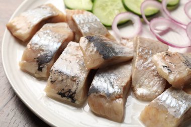 Lezzetli ringa balıkları, soğan ve salatalık dilimleri ahşap masada, yakın plan.