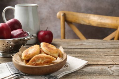 Lezzetli kızarmış pirizky (doldurulmuş turtalar) ve ahşap masada elmalar, yakın plan. Metin için boşluk