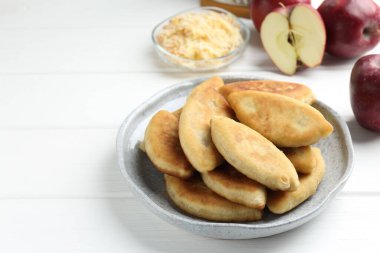 Lezzetli kızarmış pirizky (doldurulmuş turtalar) ve beyaz ahşap masada elmalar, yakın plan. Metin için boşluk