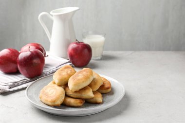 Lezzetli kızarmış pirizki (doldurulmuş turtalar), açık gri masada elmalar ve süt, yakın plan. Metin için boşluk