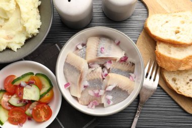 Siyah ahşap masada servis edilen soğanlı lezzetli ringa balıkları.