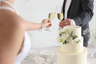 Evde düğün pastası olan evli bir çift şampanya bardaklarını tokuşturuyor.