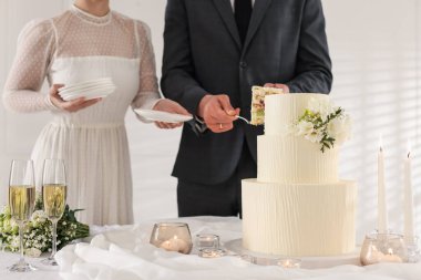 Damat düğün pastasından bir parça alırken gelin içeride masada tabakları tutuyor.