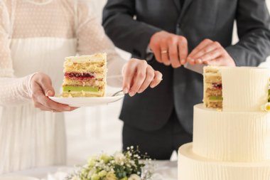 Yeni evliler kapalı bir masada düğün pastası kesiyorlar.