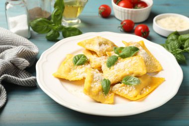 Açık mavi ahşap masada servis edilen peynirli ve fesleğenli lezzetli ravioli.