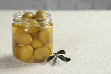 Kavanozda yeşil zeytin turşusu ve beyaz desenli masada yapraklar, yakın plan. Metin için boşluk
