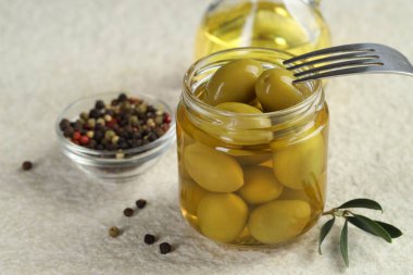 Kavanozda, çatalda, yağda ve biberli yeşil zeytinleri beyaz desenli masada, yakın plan.