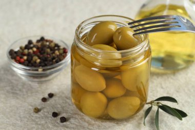 Kavanozda, çatalda, yağda ve biberli yeşil zeytinleri beyaz desenli masada, yakın plan.