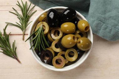 Farklı lezzetlerde marine edilmiş zeytin halkaları, bütün olanlar ve biberiyeler açık ahşap masada, düz uzanmış.