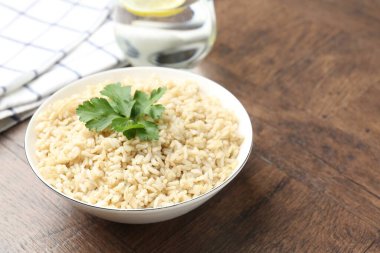 Ahşap masada servis edilen maydanozlu lezzetli kahverengi pirinç, yakın plan. Metin için boşluk