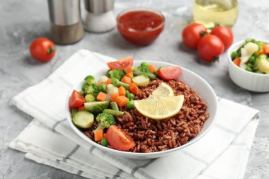 Gri desenli masada servis edilen sebzeli ve limon dilimli lezzetli kahverengi pirinç, yakın plan.