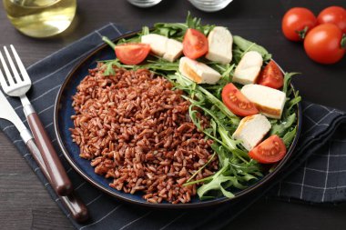 Lezzetli kahverengi pirinç, tavuk, roka ve domatesler siyah ahşap masada, yakın plan.