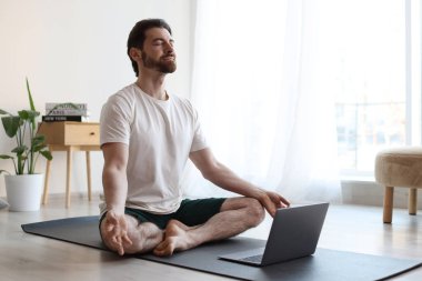 Adam evde dizüstü bilgisayarın yanında meditasyon yapıyor.