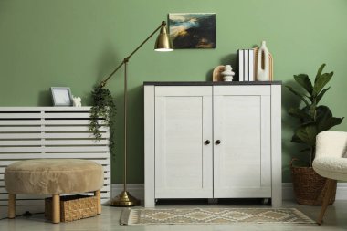 Farklı dekorlu bir dolap, yeşil duvarın yanında lamba ve puf. İç tasarım