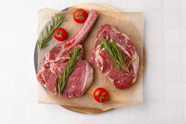 Pieces of raw beef, rosemary and tomatoes on white tiled table, top view