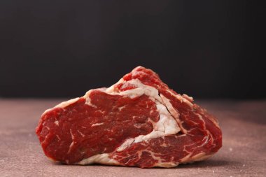 One piece of raw beef on brown textured table against black background, closeup
