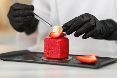 Mutfaktaki beyaz masada nefis bir tatlıyı dekore eden şekerci.