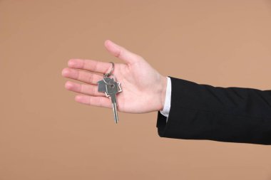 Emlakçının elinde anahtarlık bej arka planda ev şekilli anahtarlık, yakın plan.