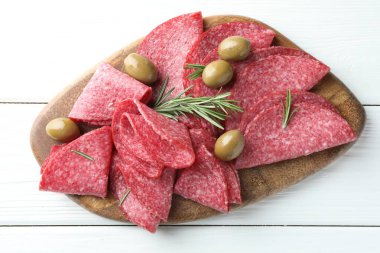 Beyaz ahşap masada servis edilen zeytinli ve biberiyeli lezzetli sosis dilimleri.