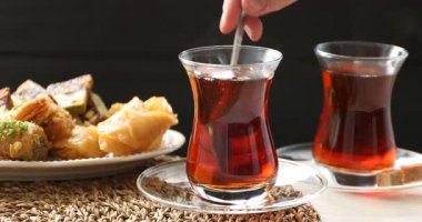 Cam fincanda kahverengi şeker ekleyen ve karıştıran bir kadın ve masada Türk çayı, yakın plan