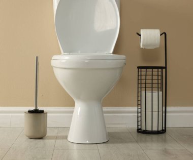 Toilet bowl, brush and necessities near beige wall in restroom