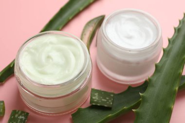 Aloe vera özütüyle nemlendirici krem ve pembe arka planda yapraklar, yakın plan.