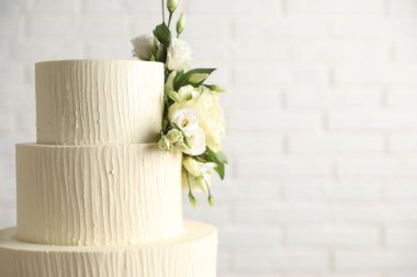 Beyaz tuğla duvarın yanında çiçeklerle süslenmiş nefis düğün pastası, yakın plan. Metin için boşluk