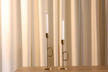 Ahşap masada yanan mumlarla bej perdelere karşı şık şamdanlar.