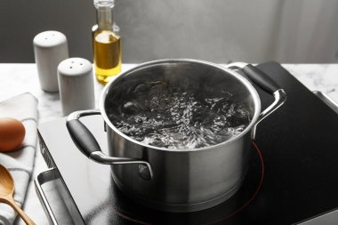 Kaynar suyla tencereyi pişirmek ve arka plandaki gri ışığa karşı soba, yakın plan