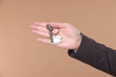 Emlakçının elinde anahtarlık bej arka planda ev şekilli anahtarlık, yakın plan.