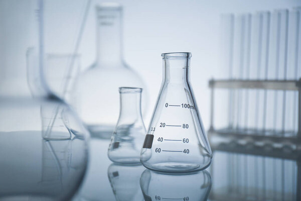Laboratory glassware on mirror surface against light background