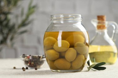 Kavanozda turşulu yeşil zeytin, beyaz desenli masada yağlı ve biberli mısır, yakın plan.