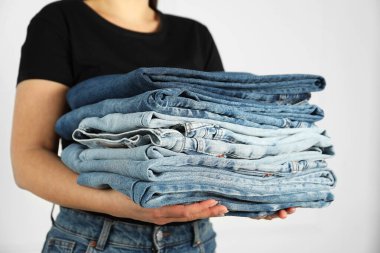 Kapalı alandaki aydınlık duvarın yanında farklı şık kot pantolonları olan kadın, yakın plan.