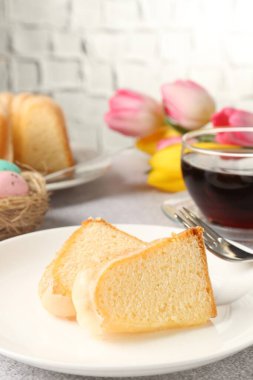 Lezzetli kek parçaları, Paskalya yumurtaları, laleler ve çay gri masada, yakın plan.