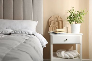 Yatağın yanında kitap, dekor ve bir bardak su olan komodin.